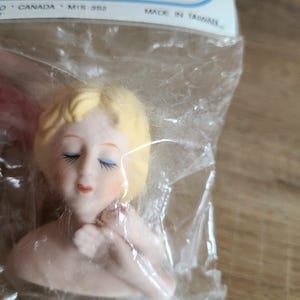 May include: A porcelain doll head with closed eyes and blonde hair. The head is in a plastic bag with a price tag that reads "3.98 Made in Taiwan".