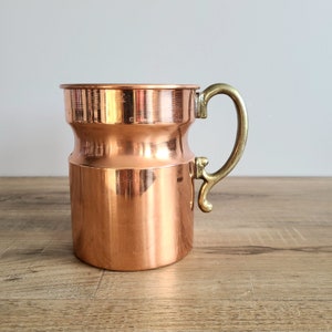Peut inclure: Une tasse en cuivre avec une poignée en laiton. La tasse a un corps arrondi et une lèvre évasée.