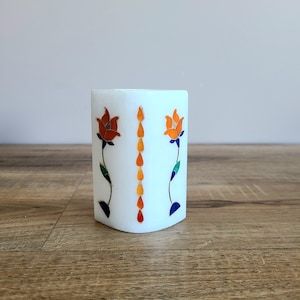 May include: White marble candle holder with a floral design. The holder features two orange flowers with green stems and leaves, and a line of orange teardrop shapes down the centre.