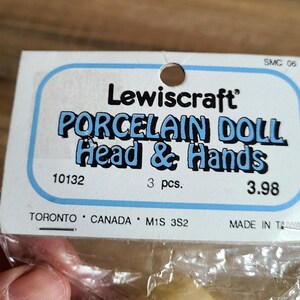 May include: A package containing three porcelain doll heads and hands. The package is white with blue text that reads "Lewiscraft Porcelain Doll Head & Hands". The package also includes the product number "10132", the quantity "3 pcs.", and the price "3.98".