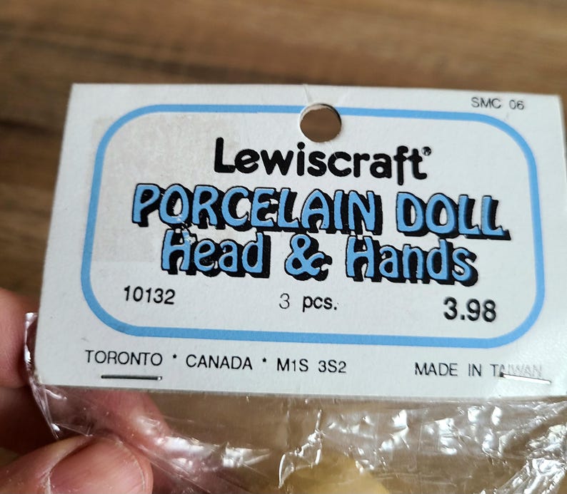May include: A package containing three porcelain doll heads and hands. The package is white with blue text that reads "Lewiscraft Porcelain Doll Head & Hands". The package also includes the product number "10132", the quantity "3 pcs.", and the price "3.98".