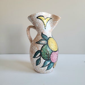 May include: A ceramic jug with a white background and a floral design in shades of green, yellow, and pink. The jug has a textured surface and a ruffled top.