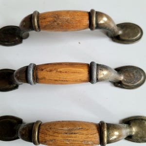May include: Three cabinet handles with a wood grain centre and antique brass finish. The handles have a curved design and are approximately 13 cm long.