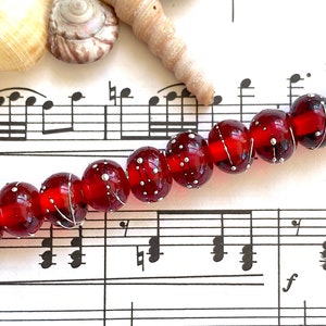 Op de afbeelding: Een streng rode glazen kralen met zilveren vlekken en witte lijnen op een blad muziek.