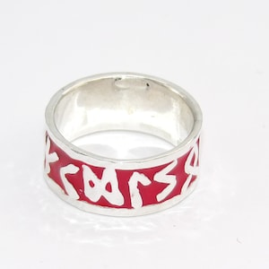 May include: A silver ring with a red enamel band and white inscription.