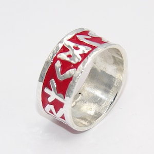 May include: A silver ring with a red band and white lettering. The lettering is in a stylised font and appears to be a word or phrase.