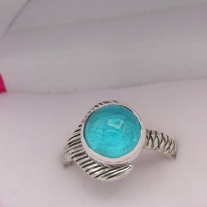 May include: A silver ring with a turquoise blue stone set in a twisted band. The ring is displayed in a pink velvet ring box.