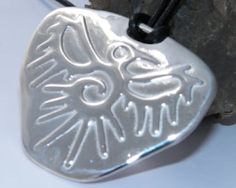 May include: A silver pendant with a stylized bird design, hanging from a black leather cord. The pendant is shaped like a teardrop and has a textured surface.