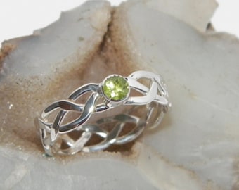 Può includere: Un anello d'argento con un designo a nodo celtico e una pietra preziosa verde al centro.