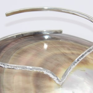 May include: A silver hammered bangle bracelet with a V-shaped opening. The bracelet is made of a thin, flexible metal and has a textured surface.
