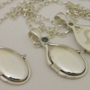 Puede incluir: Tres collares de plata con colgantes de forma ovalada. Cada colgante tiene una pequeña piedra azul en la parte superior. Un colgante tiene un diseño decorativo en la parte posterior.