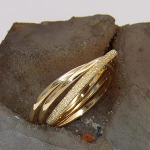 May include: A gold ring with a textured finish. The ring is made of three bands that are intertwined.