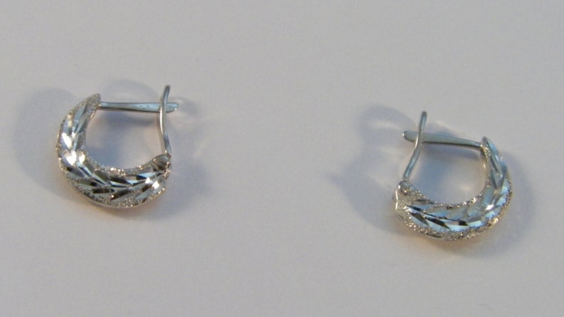 Puede incluir: Un par de pendientes de aro de plata con un patr&oacute;n de diamante. Los pendientes son peque&ntilde;os y delicados.