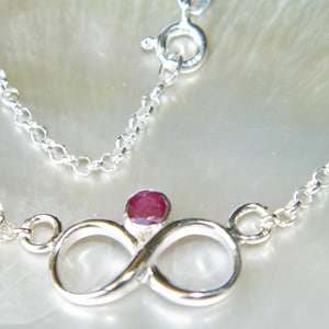 May include: A silver infinity necklace with a red gemstone in the center.