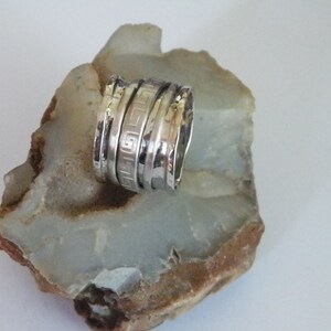 K&ouml;nnte beinhalten: Ein silberner Ring mit einer strukturierten Band und einem geometrischen Design. Der Ring besteht aus mehreren &uuml;bereinander gestapelten B&auml;ndern.