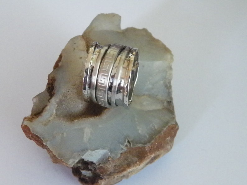 K&ouml;nnte beinhalten: Ein silberner Ring mit einer strukturierten Band und einem geometrischen Design. Der Ring besteht aus mehreren &uuml;bereinander gestapelten B&auml;ndern.