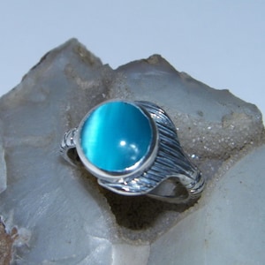 May include: A silver ring with a blue oval gemstone. The ring has a textured band.