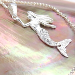 May include: A silver mermaid pendant necklace with clear crystal accents. The pendant is on a silver chain with a lobster clasp.