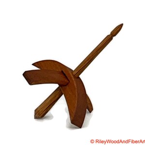 May include: A wooden drop spindle, a tool for hand spinning yarn. The spindle features a long, pointed shaft and a cross-shaped whorl. The wood has a warm, brown tone. The image is set against a white background.