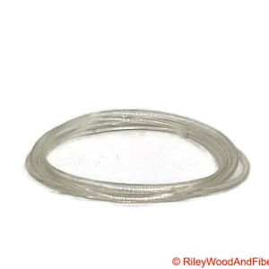 May include: A coil of clear, thin, flexible plastic tubing, arranged in a circular form. The tubing is translucent and sits against a plain white backdrop. The lighting is good, emphasising the texture and shape of the material.