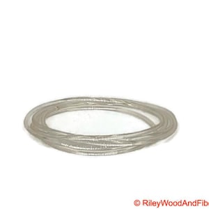 以下が含まれることがあります： 透明で細い、銀色のブレスレットの束。ブレスレットは一緒に巻かれており、円形を形成しています。画像は無地の白い背景に配置されています。ブレスレットは柔軟な素材でできているようです。