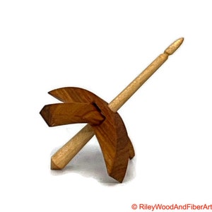 May include: A wooden spinning wheel with a spindle and a base. The spindle is made of light wood and the base is made of dark wood.