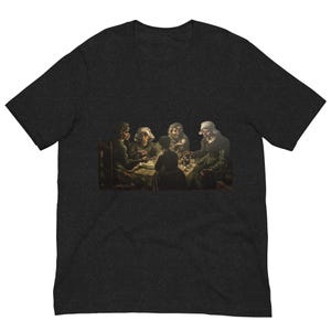 May include: Dark heather gray t-shirt featuring a print of a painting depicting a group of people seated around a table. The painting shows figures in dark clothing, illuminated by soft light, engaged in a meal. The artwork is a classic, historical piece.
