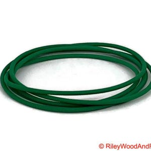 May include: A bundle of several loops of dark green elastic cord, arranged in a circular shape. The cord is a solid, vibrant green color, and appears to be made of a flexible material. The background is white.