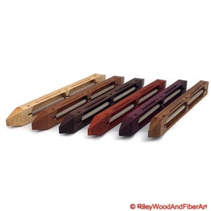 May include: A collection of seven wooden weaving shuttles in various wood tones, including light, medium, and dark browns, and a reddish-purple. Each shuttle has a central opening with a white spool of thread. The shuttles are arranged diagonally.