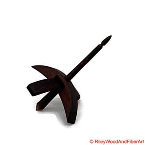 May include: A dark brown wooden drop spindle, a tool for hand spinning yarn. The spindle has a central shaft with a pointed tip and a circular whorl with three curved arms. The item is set against a white background.