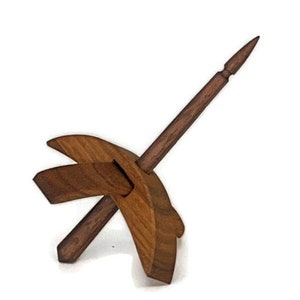 May include: A wooden drop spindle, a tool for hand spinning yarn. The spindle features a long, pointed shaft and a cross-shaped whorl. The wood has a warm, natural tone, and the design is simple and functional.