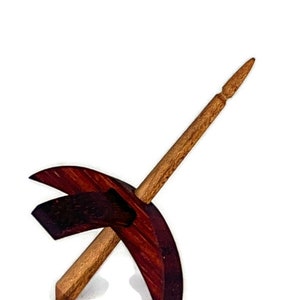 May include: A wooden drop spindle with a dark reddish-brown whorl and a lighter brown shaft. The spindle is designed for spinning fibers and has a pointed tip.