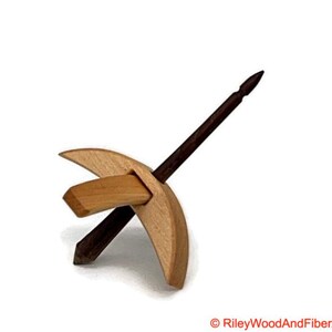 May include: A wooden drop spindle for spinning yarn. The spindle has a light-coloured, crescent-shaped whorl with a rectangular crossbar and a dark brown shaft. The design is simple and elegant, ideal for fiber art enthusiasts.