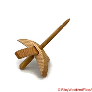 May include: A wooden drop spindle for hand spinning yarn. It has a long, thin shaft and a cross-shaped whorl. The wood is a natural, light brown colour. The design is simple and functional, a traditional tool for fibre crafts.