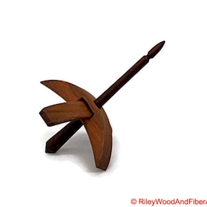 May include: A wooden drop spindle, a tool for hand spinning yarn. The spindle features a dark brown shaft and a circular whorl with a curved design. The whorl is made of a lighter brown wood. The tool is designed for fiber art and yarn making.