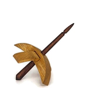 May include: A wooden spinning wheel with a dark brown spindle and a light brown base. The spindle is pointed at one end and has a small knob at the other end.