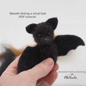 Puede incluir: Un murciélago negro de fieltro de aguja con las alas extendidas, sostenido en una mano. El murciélago es un pequeño proyecto artesanal detallado. La imagen incluye el texto "Needle felting a small bat PDF tutorial" y "detailed instructions by Melkada".