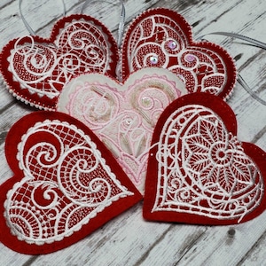 May include: Five red felt hearts with white lace embroidery. The hearts are decorated with white beads and sequins.