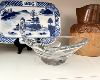 May include: A clear glass bowl with a unique, wavy design. The bowl is shaped like a crescent moon and has a smooth, polished finish.