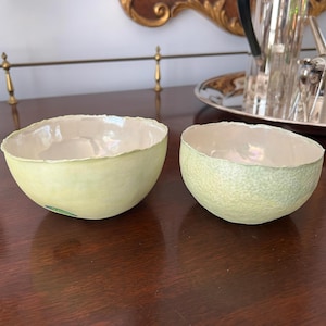 May include: Two pale green ceramic bowls with a textured surface. The bowls are sitting on a wooden table.