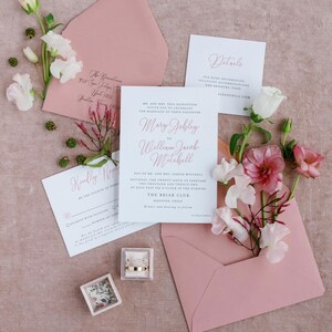 Puede incluir: Un conjunto de invitaciones de boda en rosa y blanco con un sobre rosa, una tarjeta de invitación blanca con caligrafía rosa, una tarjeta RSVP blanca y una tarjeta de detalles blanca. La tarjeta de invitación presenta los nombres Mary Ashley y William Jacob Mitchell, la fecha sábado 26 de febrero de 2022 y la hora 18:30. La tarjeta de invitación también incluye la ubicación, The Briar Club, Houston, Texas.