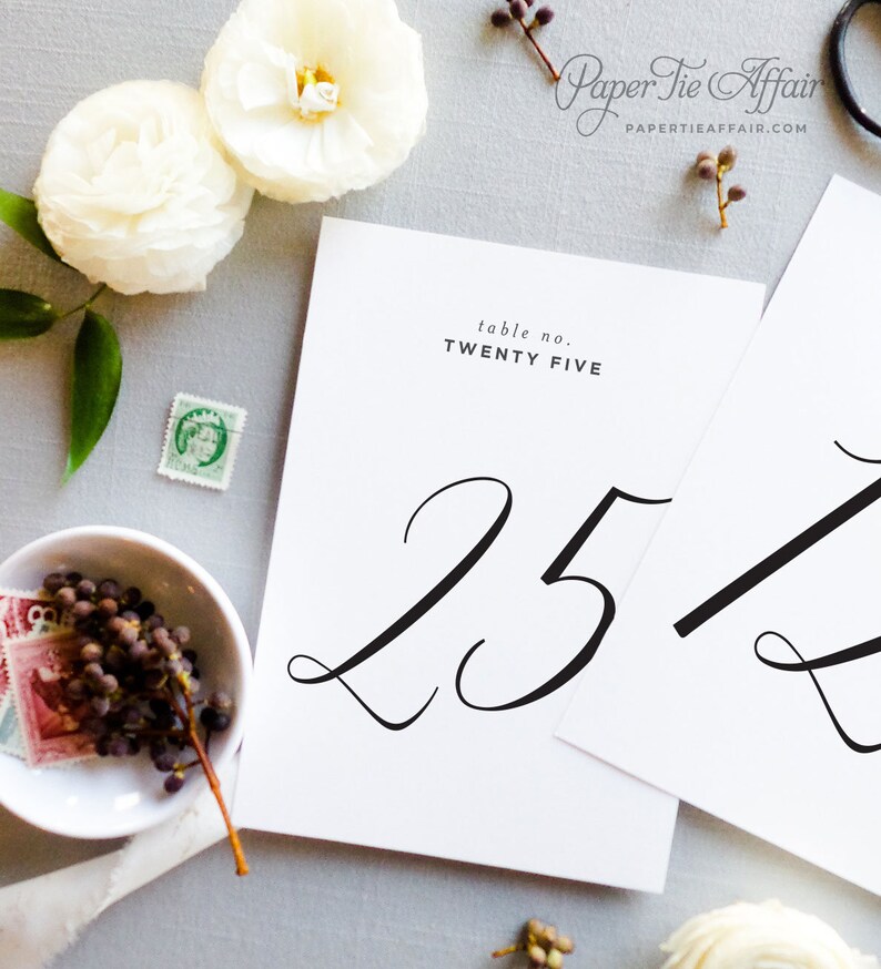 Peut inclure: Carte blanche avec calligraphie noire pour le num&eacute;ro de table vingt-cinq. Le texte "table no. TWENTY FIVE" est imprim&eacute; en noir en haut de la carte.