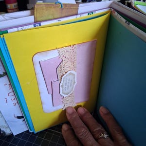 Pu&ograve; includere: Una pagina di scrapbooking fatta a mano con uno sfondo giallo brillante, un inserto in cartoncino rosa e una striscia di pizzo beige. Una piccola etichetta di carta smerlata &egrave; fissata al pizzo con il testo, Grow through what you go through.