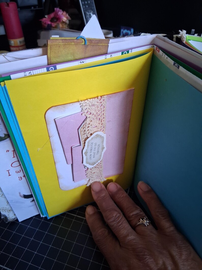 Pu&ograve; includere: Una pagina di scrapbooking fatta a mano con uno sfondo giallo brillante, un inserto in cartoncino rosa e una striscia di pizzo beige. Una piccola etichetta di carta smerlata &egrave; fissata al pizzo con il testo, Grow through what you go through.