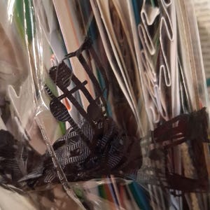 Pu&ograve; includere: Un oggetto in plastica nera stampato in tre dimensioni con una complessa struttura a reticolo aperto, caratterizzato da sottili montanti verticali e orizzontali interconnessi, racchiuso in una custodia di imballaggio in plastica trasparente e stropicciata.