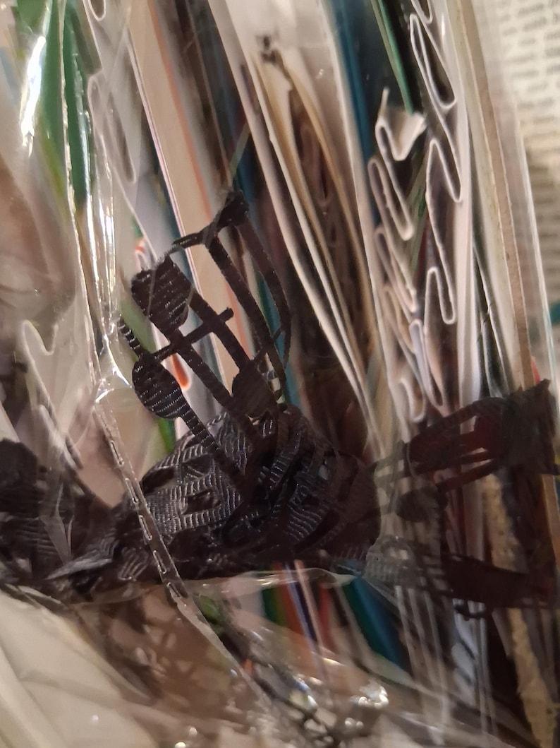 Pu&ograve; includere: Un oggetto in plastica nera stampato in tre dimensioni con una complessa struttura a reticolo aperto, caratterizzato da sottili montanti verticali e orizzontali interconnessi, racchiuso in una custodia di imballaggio in plastica trasparente e stropicciata.
