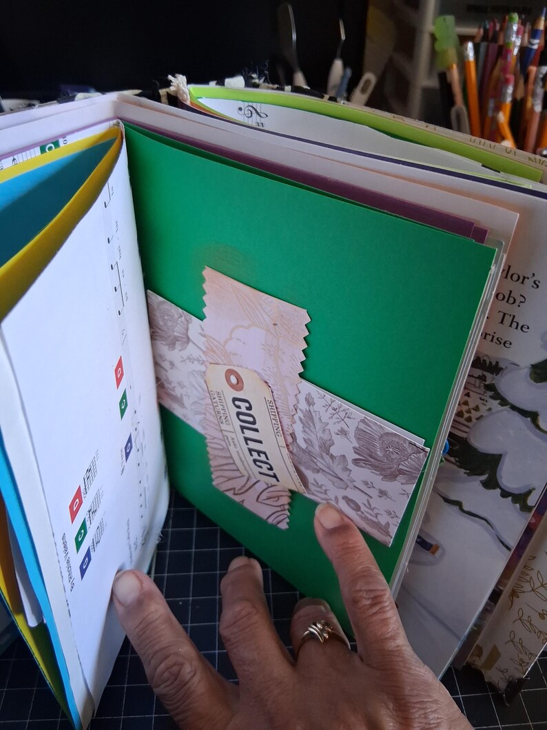 Pu&ograve; includere: Una pagina di scrapbooking con un foglio di carta verde brillante e una striscia decorativa a motivi floreali rosa al centro. Un piccolo cartellino beige con la parola COLLECT stampata in nero &egrave; fissato alla striscia. Fa parte di un libro.