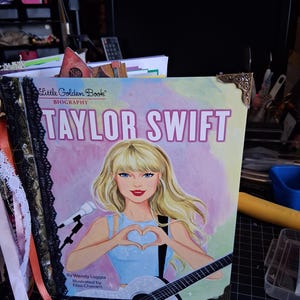 Pu&ograve; includere: Una biografia Little Golden Book di Taylor Swift con una copertina illustrata in cui l'artista forma un cuore con le mani, tiene una chitarra ed &egrave; accanto a un microfono. Il libro presenta finiture in pizzo nero e angoli in metallo dorato.