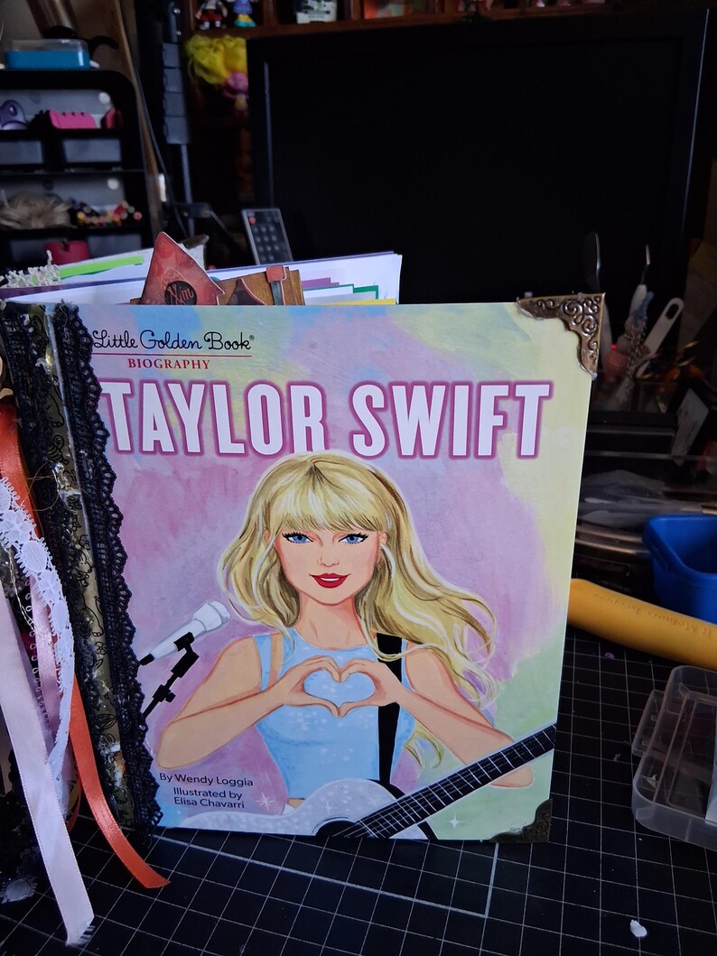Pu&ograve; includere: Una biografia Little Golden Book di Taylor Swift con una copertina illustrata in cui l'artista forma un cuore con le mani, tiene una chitarra ed &egrave; accanto a un microfono. Il libro presenta finiture in pizzo nero e angoli in metallo dorato.