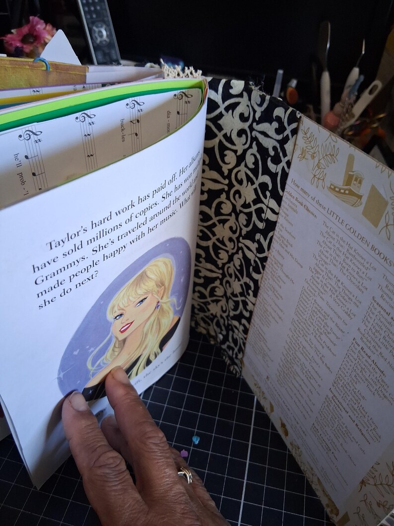 Pu&ograve; includere: Un libro con il dorso a motivo damascato bianco e nero e una pagina con l'illustrazione di un personaggio biondo. Il testo recita: Taylor's hard work has paid off. Her albums have sold millions of copies. She has won many Grammys. She's traveled around the world and made people happy with her music. What will she do next?